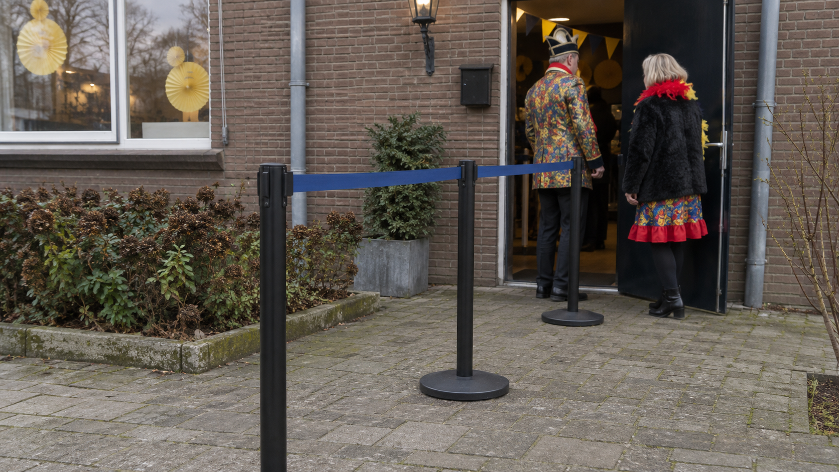 Afzetpaaltjes met blauwe linten bij de ingang van een carnavalsbijeenkomst.