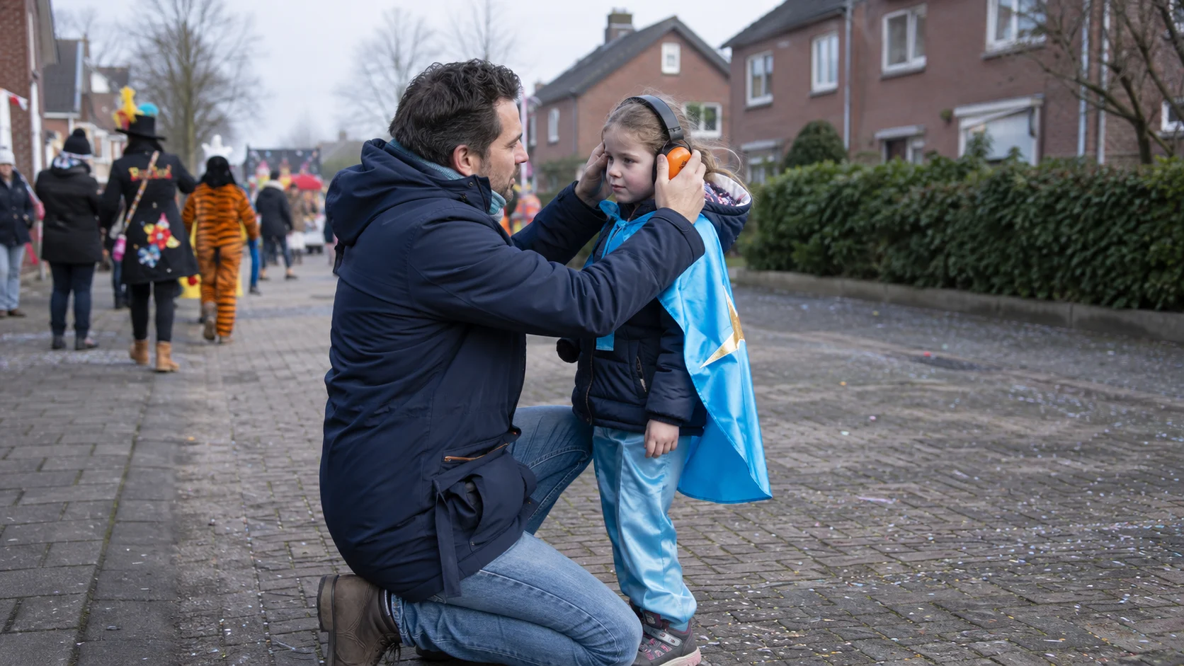Vader helpt zijn verklede dochter met oranje gehoorbescherming langs de carnavalsroute