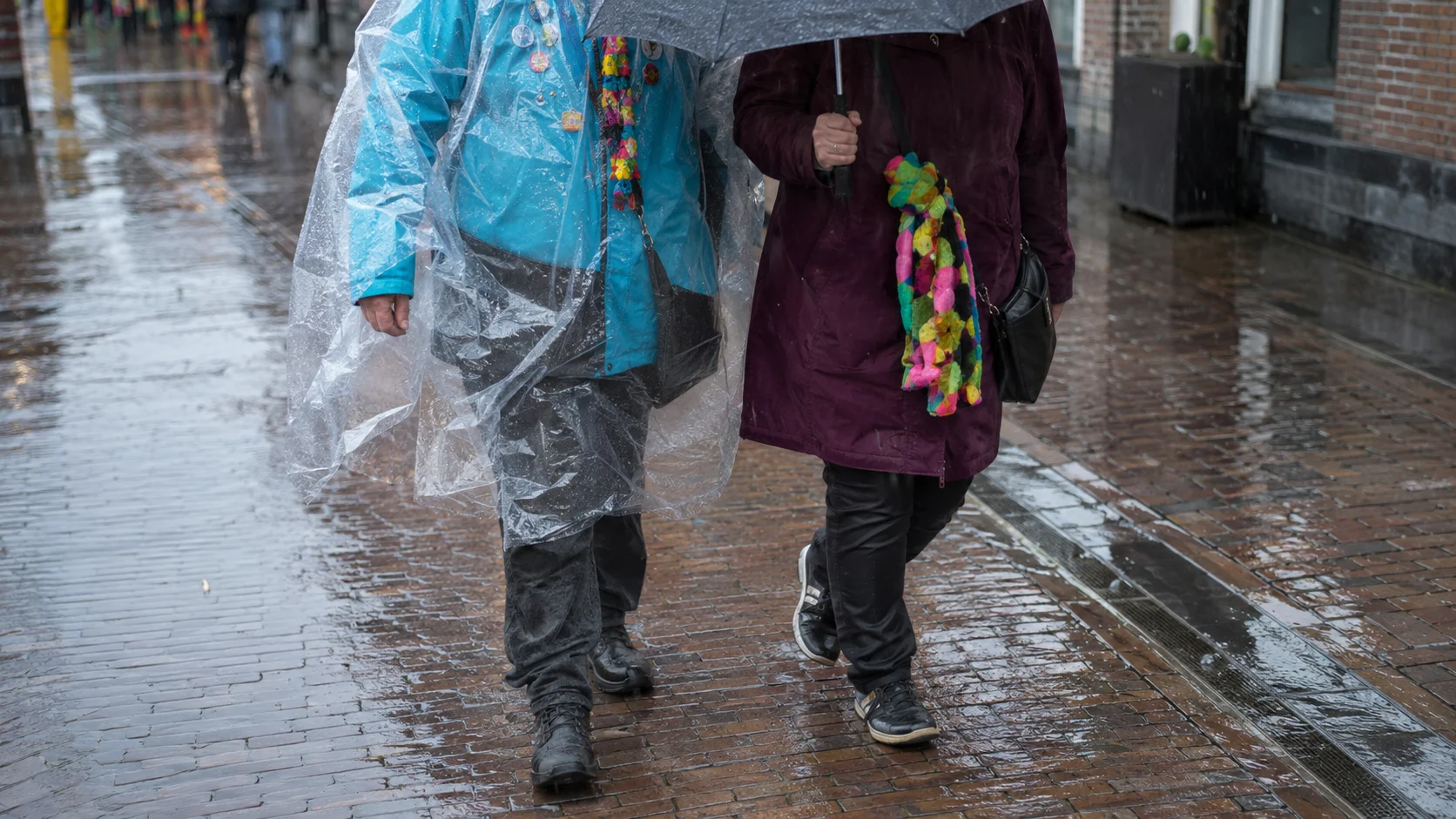 Carnavalsoutfits met regenponcho, paraplu en stevige schoenen op natte straatstenen